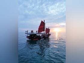 A vibrant sunset scene featuring a group enjoying a boat party on a traditional vessel, with paddleboarding and swimming in the serene waters.