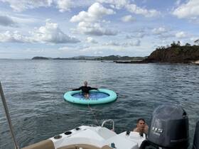 Two individuals enjoy a relaxing day on the water, one lounging on a floating mat while the other swims nearby — a perfect scene for summer fun and leisure.