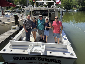 A cheerful group of friends poses aboard the 'Endless Summer' boat in Annapolis, capturing a moment of fun and camaraderie on the water.