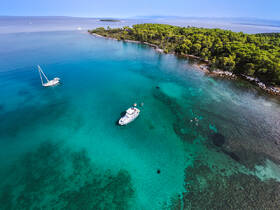 A stunning aerial view of two boats anchored in crystal-clear waters, with people snorkeling nearby, showcasing the beauty of the island and its vibrant marine life.