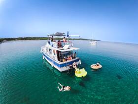 A lively group enjoys a day on the water, swimming and relaxing around a boat with inflatable toys in crystal-clear waters — perfect for summer fun and aquatic adventures.