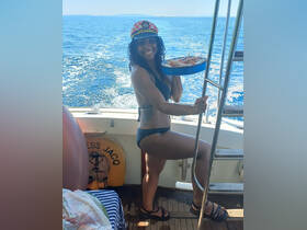 A joyful woman in a captain's hat serves delicious seafood on a boat, capturing the essence of a fun day at sea.