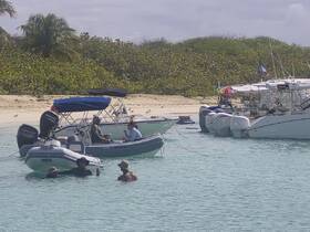 A lively scene of people enjoying a day on the water, swimming and relaxing near their boats at a beautiful beach destination.