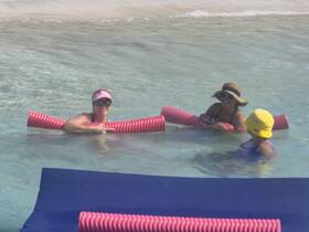 A group of friends enjoys a fun day in the shallow waters, relaxing with pool noodles at the beach — perfect for a summer getaway.