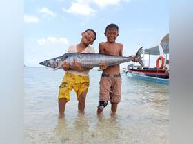 Two joyful children proudly display their catch of the day, a large fish, while standing in shallow water — a delightful moment capturing the thrill of fishing.