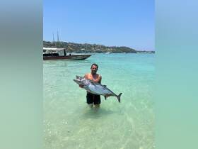 A man proudly displays his impressive catch while standing in shallow waters, showcasing the thrill of fishing in a beautiful ocean setting.