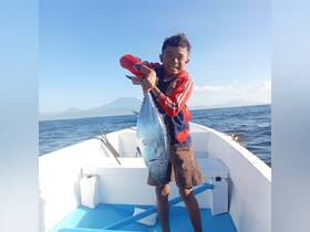 A young boy proudly displays his catch while fishing on a boat, showcasing the excitement of a successful day on the water.