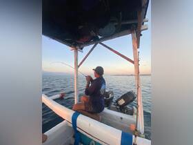 A fisherman casts his line from a small boat during a picturesque sunset, capturing the essence of a tranquil fishing experience on the open water.