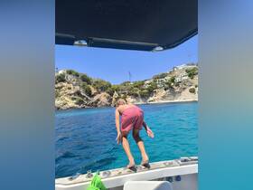 A child prepares to jump into the crystal-clear waters from the side of a boat, capturing the excitement of summer adventures on the water.