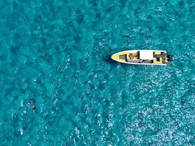 An aerial view captures a vibrant scene of a boat with guests enjoying the turquoise waters, while a swimmer adds to the lively atmosphere — perfect for summer adventures.
