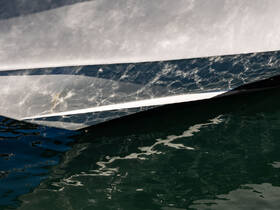 A close-up view of a boat's hull reflecting the shimmering water, showcasing the sleek design and craftsmanship of the vessel.