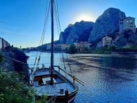 A serene view of a docked yacht along a tranquil river, framed by majestic mountains and charming buildings, perfect for showcasing the beauty of waterfront landscapes.