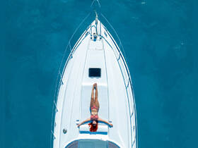 An aerial view of a woman sunbathing on the deck of a boat, surrounded by stunning turquoise waters — a perfect scene for relaxation and summer escapes.