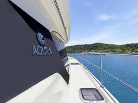 A close-up view of the side of an Aquila yacht, showcasing its sleek design against a serene backdrop of blue waters and lush greenery.