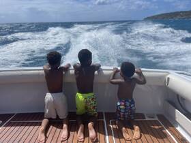 Three children enjoy the thrill of the ocean breeze while kneeling on the deck of a boat, creating unforgettable family memories on the water.