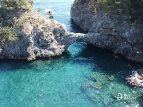 A stunning aerial view of a secluded cove with crystal-clear waters, featuring a boat anchored nearby and a swimmer enjoying the serene surroundings — perfect for exploring hidden gems on the water.