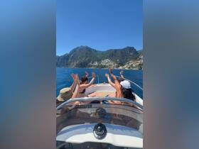 A group of friends joyfully waves from the deck of a boat, surrounded by stunning mountain views and sparkling ocean waters — a perfect moment of celebration on the water.