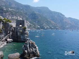 A stunning view of the Amalfi Coast featuring rocky cliffs, a historic tower, and numerous boats dotting the turquoise waters — a perfect destination for scenic boat tours.
