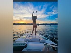 A woman celebrates at sunset on the bow of a boat, creating a vibrant atmosphere perfect for summer adventures on the water.