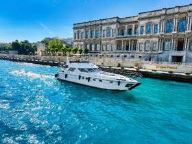 A sleek yacht glides through the vibrant turquoise waters near the historic Çırağan Palace, showcasing a perfect blend of luxury and scenic beauty.