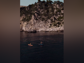 Two individuals paddleboard in serene waters against a stunning rocky coastline, capturing the essence of adventure and natural beauty.