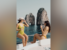 Two friends enjoy cocktails on the deck of a yacht, with stunning rock formations in the background — a perfect moment for relaxation and celebration on the water.