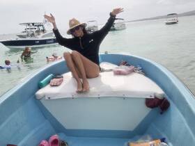 A joyful moment on the water as a woman poses on the bow of a boat, surrounded by friends enjoying the sun and swimming — perfect for a fun day out on the water.