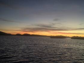 A breathtaking sunset over tranquil waters, framed by lush hills and a serene coastline — a perfect backdrop for evening boat trips.