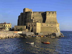 A scenic view of a historic castle by the water, surrounded by small boats and a picturesque shoreline.
