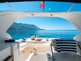 A serene view from the interior of a boat, featuring a dining area set with drinks and snacks, perfect for enjoying the tranquil waters and stunning mountain backdrop.