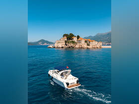 A sleek speedboat named 'Fortuna' navigates the clear blue waters near a picturesque coastal village, showcasing the beauty of the landscape and the vessel.
