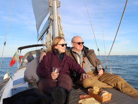 A couple enjoys a relaxing moment on a sailboat, sipping cocktails and sharing snacks while taking in the beautiful views — perfect for romantic sailing experiences.