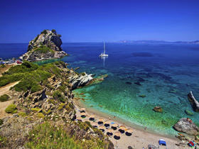 A stunning aerial view of a serene beach with a sailboat anchored nearby, showcasing the beauty of the coastline and inviting crystal-clear waters — perfect for a relaxing day on the water.