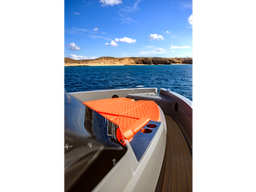 A sleek view of a boat's side deck featuring an orange sun pad, set against a backdrop of clear blue waters and sandy shores — perfect for enjoying a day on the water.