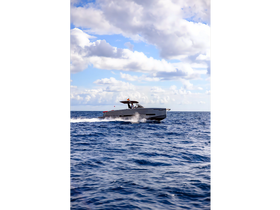 A sleek speedboat glides through the open water, showcasing its modern design against a backdrop of fluffy clouds and blue skies.