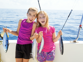 Two excited girls proudly display their catch of the day while fishing on a boat, capturing the joy of a family fishing adventure.