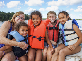 A joyful group of children and an adult pose together on a boat, all wearing life jackets, capturing a fun family boating experience.