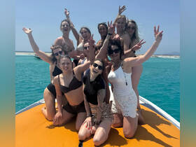 A lively group of friends celebrates on a boat, enjoying the sun and turquoise waters — perfect for a fun day out on the water.