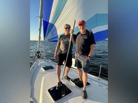Two friends enjoy a sailing adventure, posing on the deck of a sailboat with a colorful spinnaker in the background — a perfect moment for sailing enthusiasts.