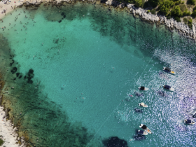 Aerial view of a vibrant beach scene with people swimming in crystal-clear turquoise waters, surrounded by boats — a perfect destination for summer fun and relaxation.