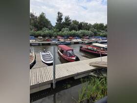 A serene view of various boats docked along a wooden pier, surrounded by lush greenery — perfect for a peaceful day on the water.