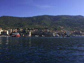 A picturesque view of a coastal town with charming architecture and boats docked along the harbor, set against a backdrop of lush green hills.