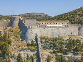 An aerial view of a historical fortress surrounded by lush greenery and hills, showcasing the architectural features of the structure.