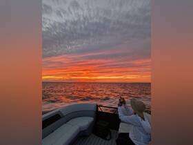 A guest captures the stunning sunset from the deck of a boat, showcasing vibrant colors over the water — an ideal moment for photography enthusiasts on evening cruises.