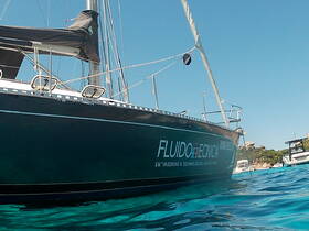 A striking side view of a yacht named 'FLUIDO ECTNICA' anchored in clear turquoise waters, showcasing its sleek design and sailing capabilities.