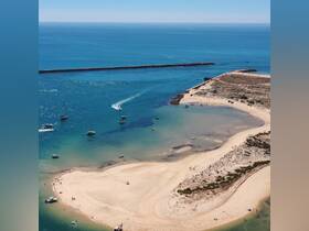 A stunning aerial view of a sandy beach and sandbar, with boats anchored nearby and people enjoying the sun — a perfect scene for beachgoers and water enthusiasts.