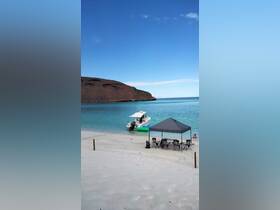 A scenic beach scene featuring a boat anchored near the shore, with guests relaxing under a canopy and a child playing in the water — perfect for a day of fun and relaxation on the coast.