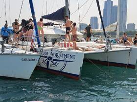 A lively group enjoys a fun day on the catamaran 'Latitude Adjustment' with city skyline in the background, perfect for summer parties and water activities.