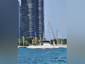 A catamaran named 'Latitude Adjustment' is seen cruising in a marina, surrounded by tall buildings and other boats, showcasing a vibrant day on the water.