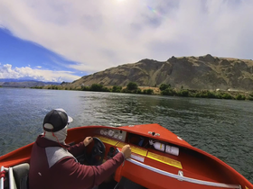 A person navigates a boat along a scenic river, surrounded by stunning landscapes and hills — perfect for adventure seekers and nature lovers.
